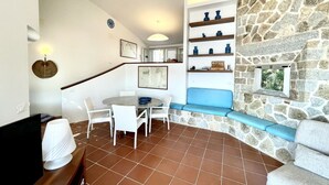 Ein Essbereich mit einem runden Tisch, Stühlen, einer blauen gepolsterten Bank und einer Steinwand mit Regalen.