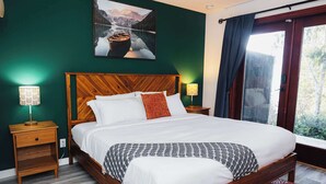 Un letto rifatto con lenzuola bianche e una coperta decorata, una testiera in legno e un comodino con una lampada.