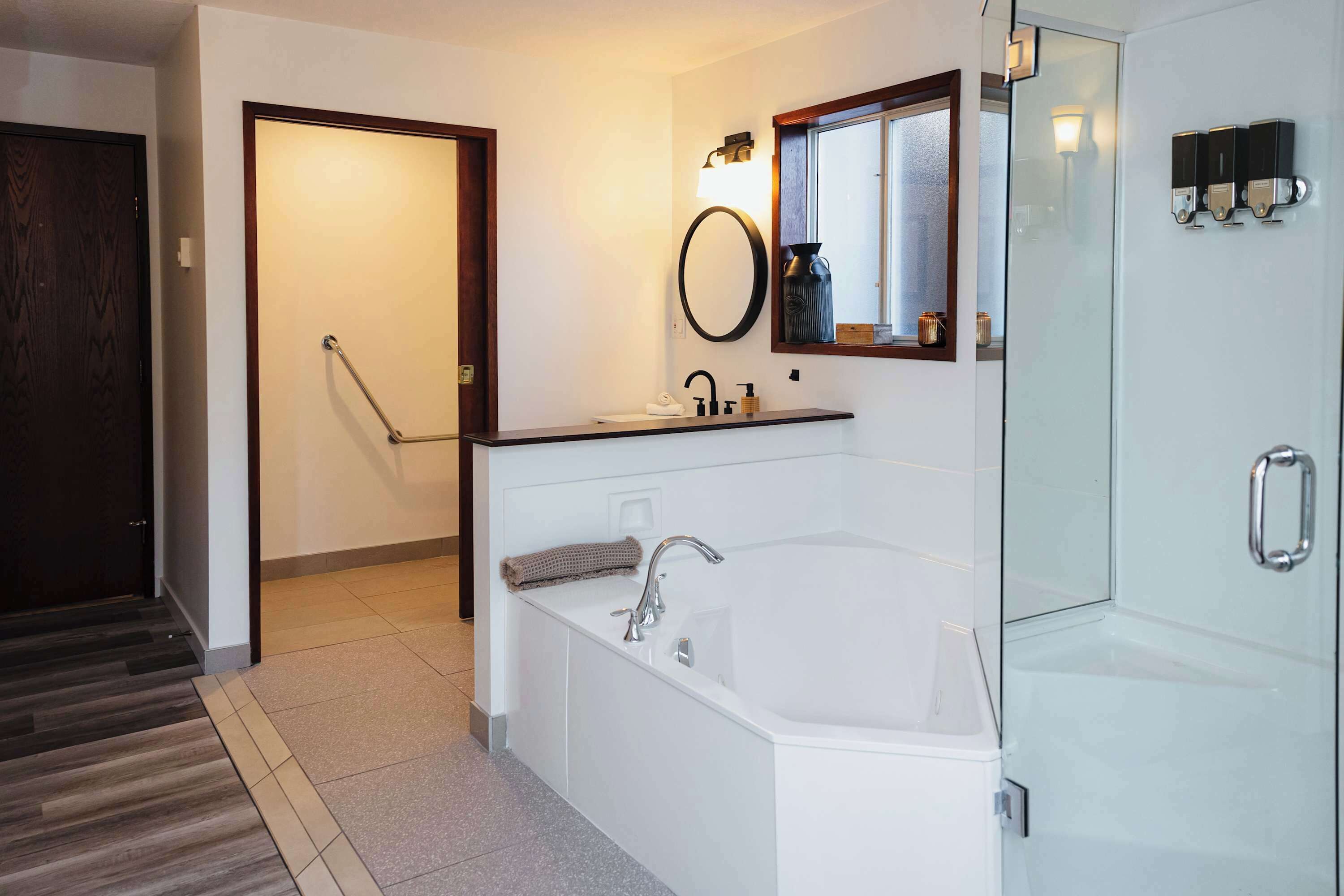 Un baño moderno con una bañera blanca grande, cabina de ducha con mampara de vidrio y tocador con espejo e iluminación.