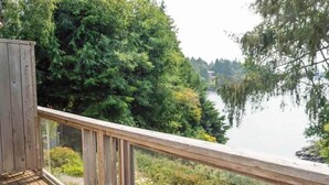 A wooden deck with a glass railing overlooking a lake, surrounded by dense greenery. - Tofino Oceanfront Hotel Suite (Tofino)
