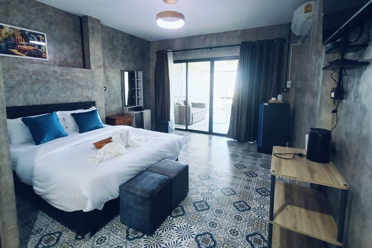 A modern hotel room with a large bed, a small desk, a TV, and a balcony with curtains.
