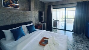A hotel room with a large bed, a painting on the wall, a desk, and a view of the outside through a glass door.