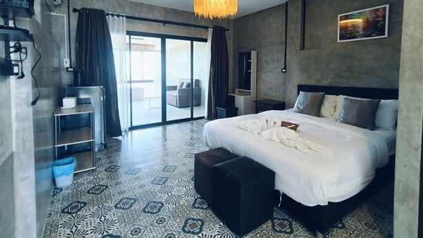 A modern hotel room with a large bed, a desk, and a balcony with a view.