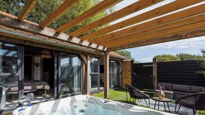 A hot tub under a wooden pergola with glass doors leading to a bedroom. - Romantic Countryside Lodge with Hot Tub (South Mundham)