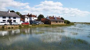 A riverside property with white buildings, parked cars, and a calm water body. - Romantic Countryside Lodge with Hot Tub (South Mundham)