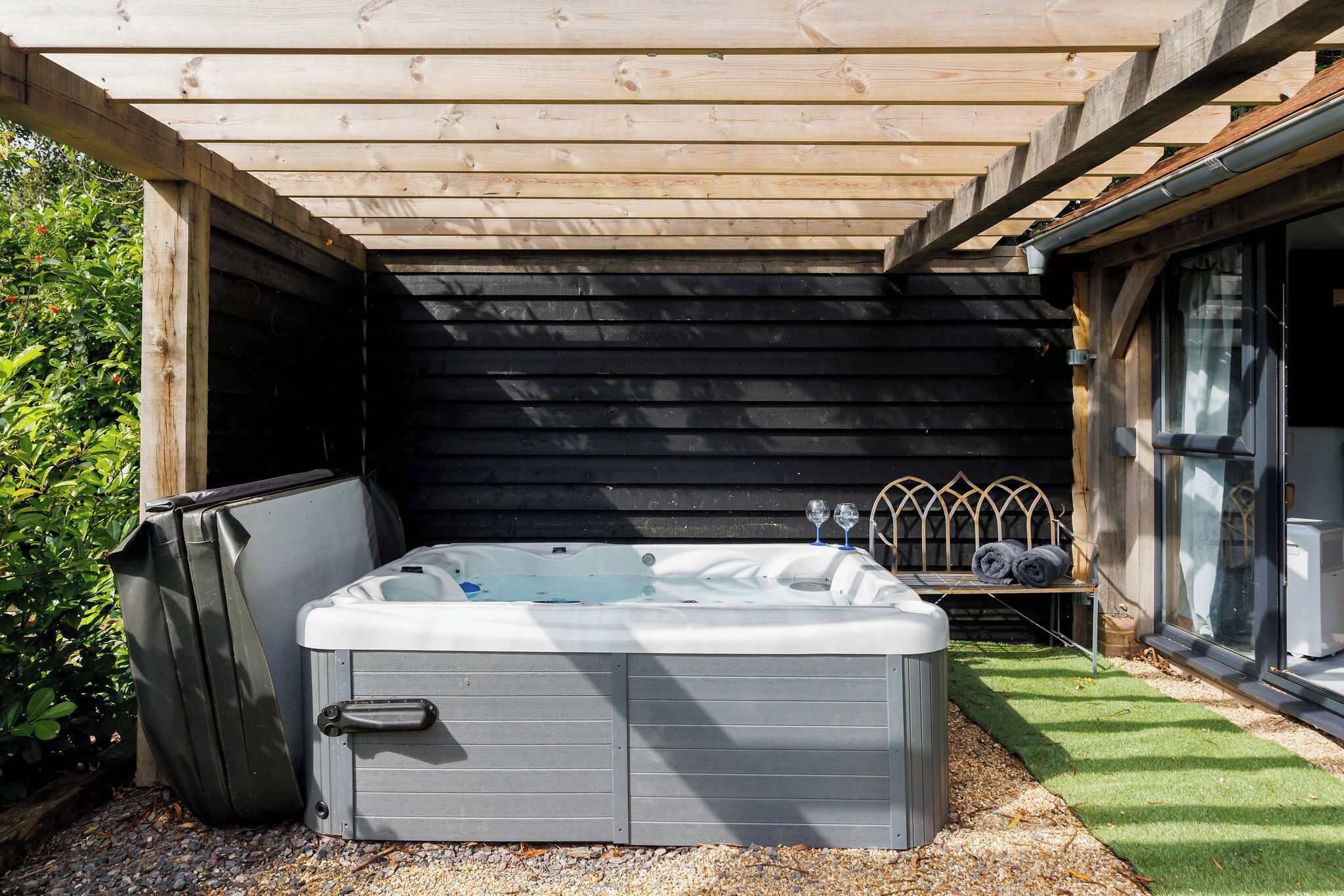 A hot tub in a covered outdoor area with a wooden ceiling, a bench, and a window.