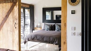 A bedroom with a large bed, a wooden door, a window, and a wall clock. - Romantic Countryside Lodge with Hot Tub (South Mundham)