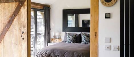 A bedroom with a large bed, a wooden door, a window, and a wall clock.
