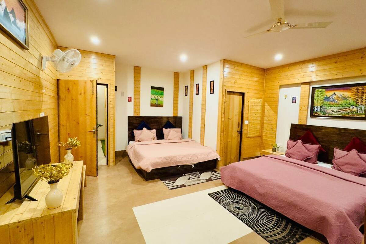 A cozy bedroom with two beds, wooden walls, a flat-screen TV, and a ceiling fan.