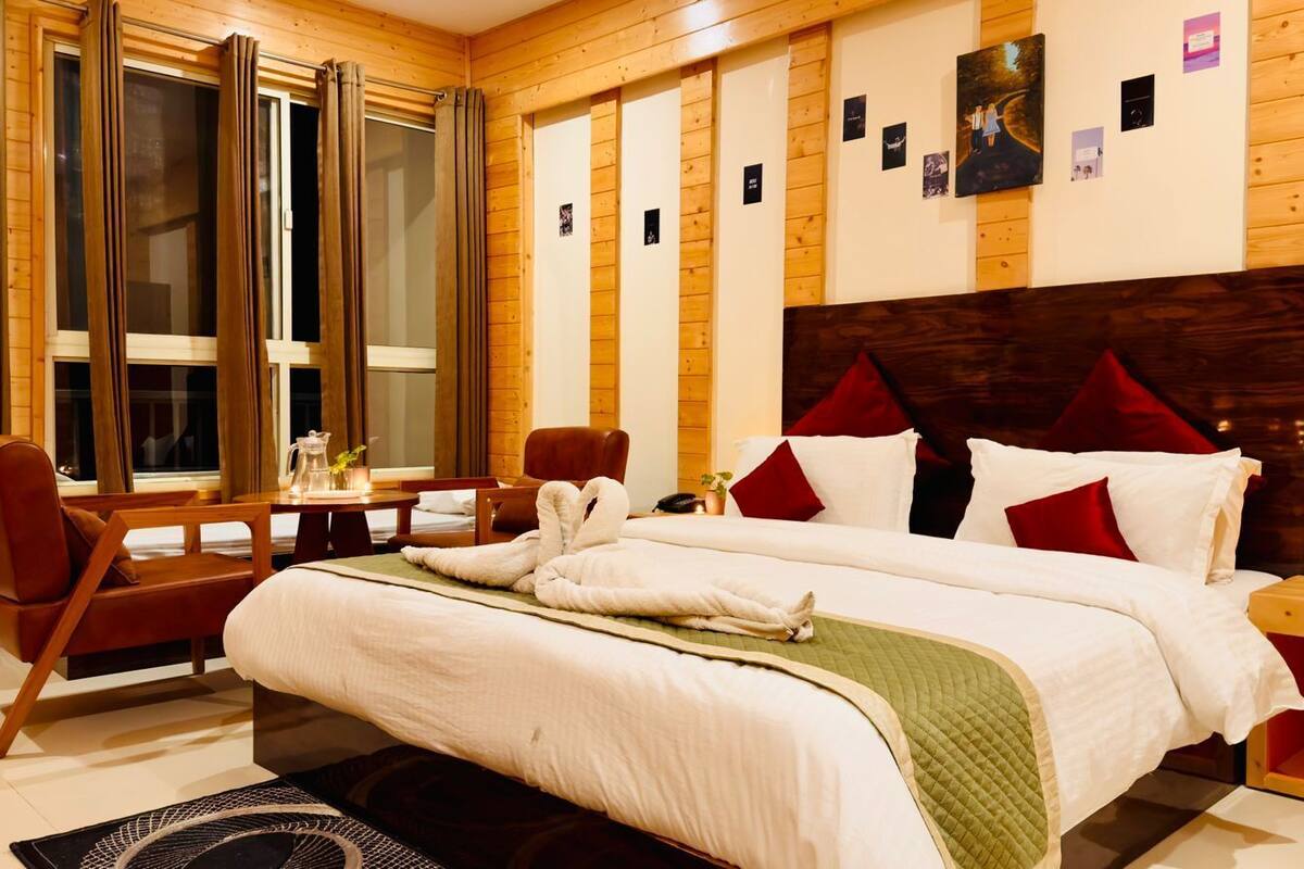 A hotel room with a large bed, two chairs, a small table, and a window with curtains.
