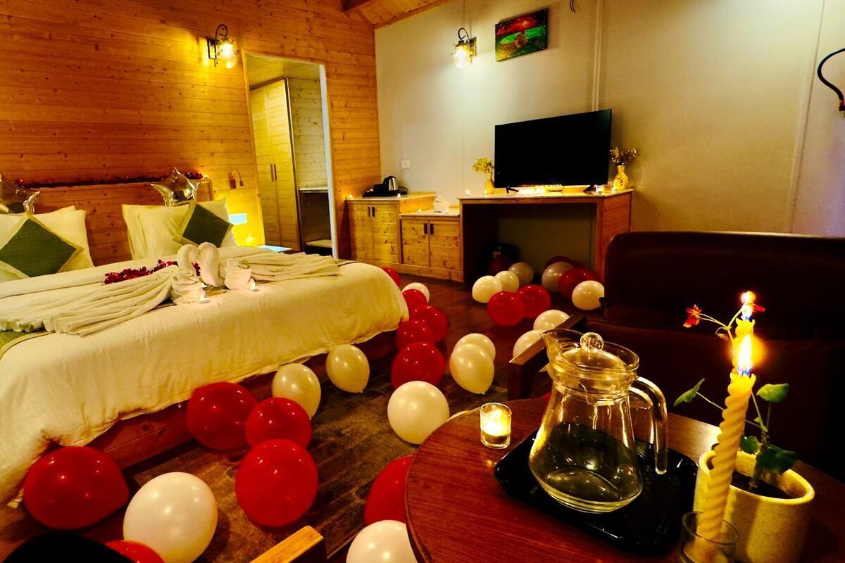 A cozy room with a bed, a TV, and a dining area with balloons and candles.