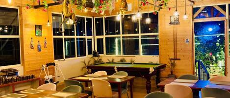 A cozy bar area with a pool table, wooden walls, and hanging plants.