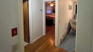A hallway with wooden flooring leading to a bedroom with a bed and a chair.