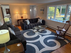 A living room with a sofa, a glass coffee table, a wooden side table, a lamp, and a rocking chair.