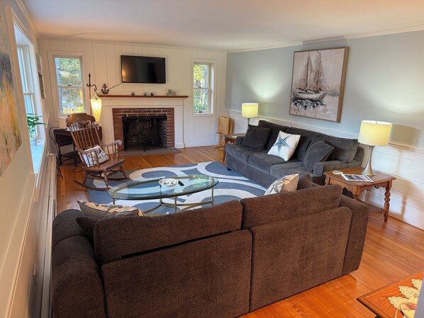 A living room with a fireplace, a television mounted above it, a sofa, a coffee table, and a painting on the wall.