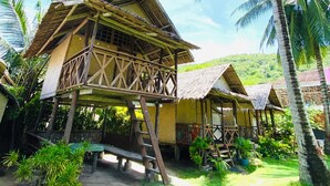 A traditional wooden structure with a thatched roof, surrounded by lush greenery and palm trees. - Ocam Ocam Casadyan Inn (Busuanga)