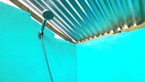 A shower area with a hose and a handheld showerhead, a wall with a teal color, and a corrugated metal ceiling. - Ocam Ocam Casadyan Inn (Busuanga)