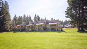 Um hotel de vários andares com telhado plano, rodeado por um gramado bem cuidado e árvores altas.