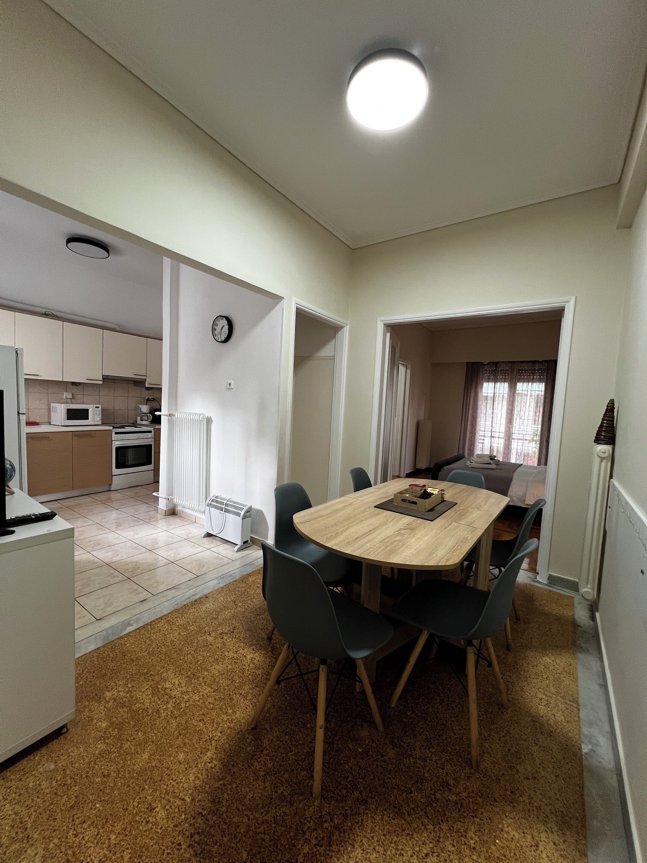 Une cuisine compacte dotée d’appareils électroménagers modernes, un coin repas avec une table et des chaises en bois, et une horloge visible au mur.