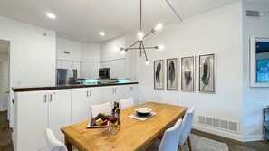 Une cuisine moderne avec des meubles blancs, une table à manger en bois et un lustre.