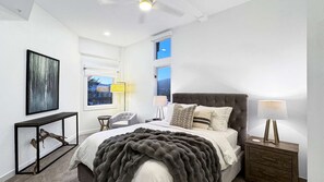 Une chambre à coucher moderne avec un grand lit, une table de chevet, une chaise et des œuvres d’art accrochées aux murs.