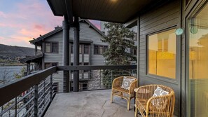 Un balcon avec deux fauteuils en osier, une vue sur un immeuble et une horloge au mur.