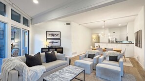 Un salon moderne avec un canapé, des fauteuils et une table basse. On y trouve également un coin repas avec une table et des chaises, ainsi qu’une cuisine équipée de meubles et d’appareils électroménagers.