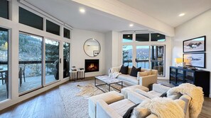 Ein großzügiges Wohnzimmer mit Kamin, großen Fenstern und Blick ins Freie.