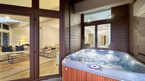 Een bubbelbad in een kamer met houten wanden en een schuifdeur naar een zithoek met een bank en een lamp.