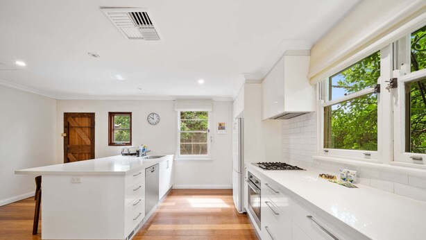 A modern kitchen with white cabinetry, a central island, and a large window providing natural light.