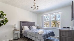 A bedroom with a bed, bedside tables, a desk, a chandelier, and a window. - Lake Front | 5 Bedroom | Fire Pit | Pet Friendly (Tobyhanna)
