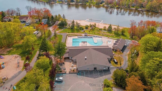 An aerial view of a lakeside property with a swimming pool, a parking lot, and surrounding trees. - Lake Front | 5 Bedroom | Fire Pit | Pet Friendly (Tobyhanna)