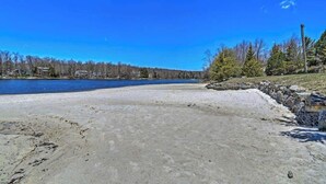 A beach with a clear sky, a body of water, and a forested area in the background. - Lake Front | 5 Bedroom | Fire Pit | Pet Friendly (Tobyhanna)