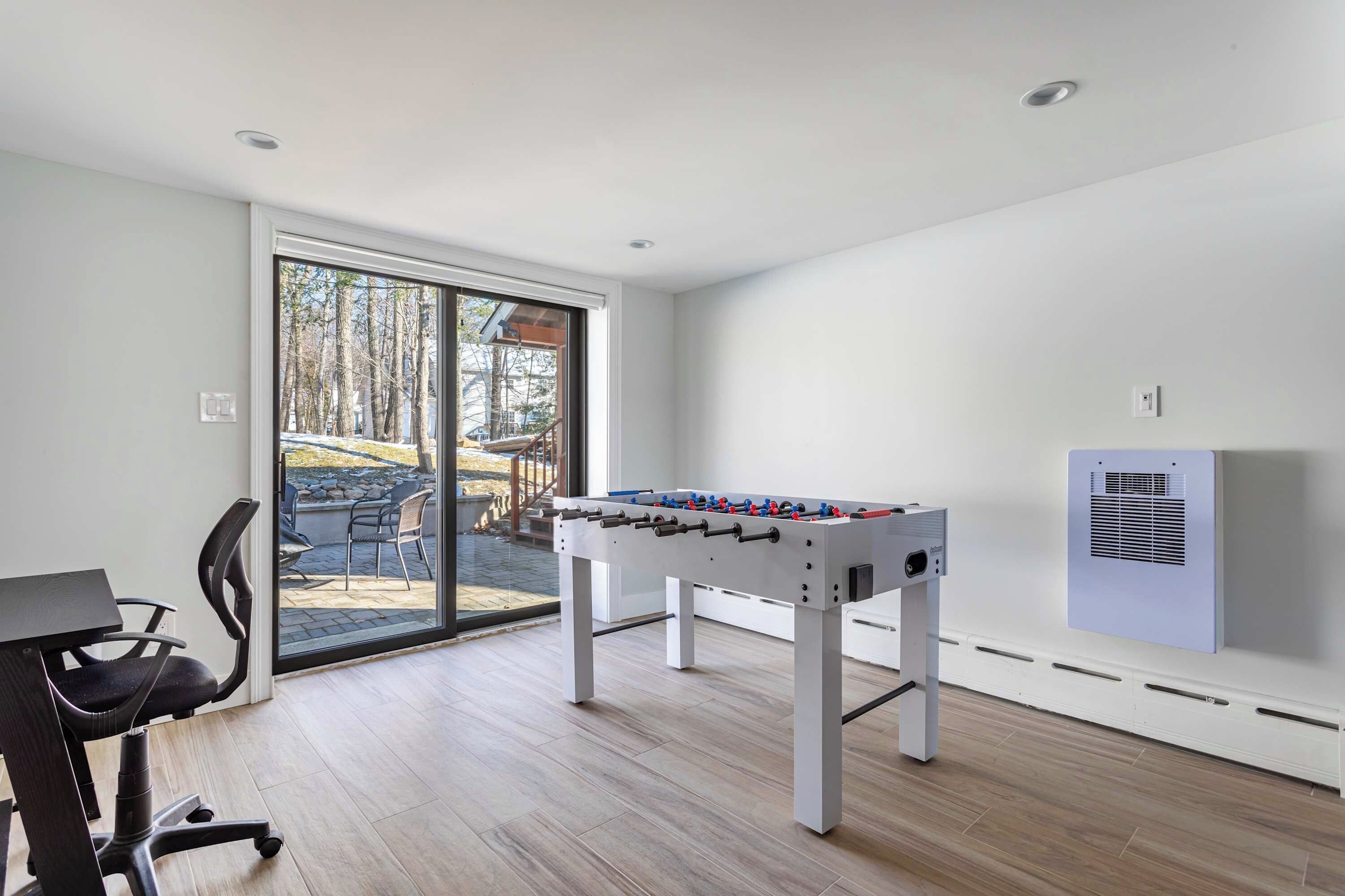 Una habitación con mesa de fútbol, escritorio y silla, y puerta corrediza de vidrio que da a un espacio exterior.
