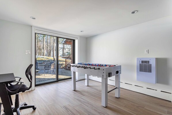A room with a foosball table, a desk with a chair, and a sliding glass door leading to an outdoor area.