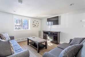 A living room with a sofa, a coffee table, a fireplace, and a TV mounted on the wall. - The Woodland Escape | Pool Table | Fire Pit | 4 BD (Tobyhanna)