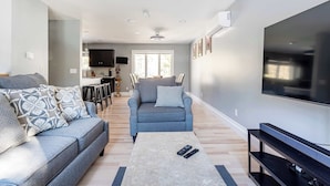 A modern living room with a grey sofa, a coffee table, and a flat-screen TV. - The Woodland Escape | Pool Table | Fire Pit | 4 BD (Tobyhanna)