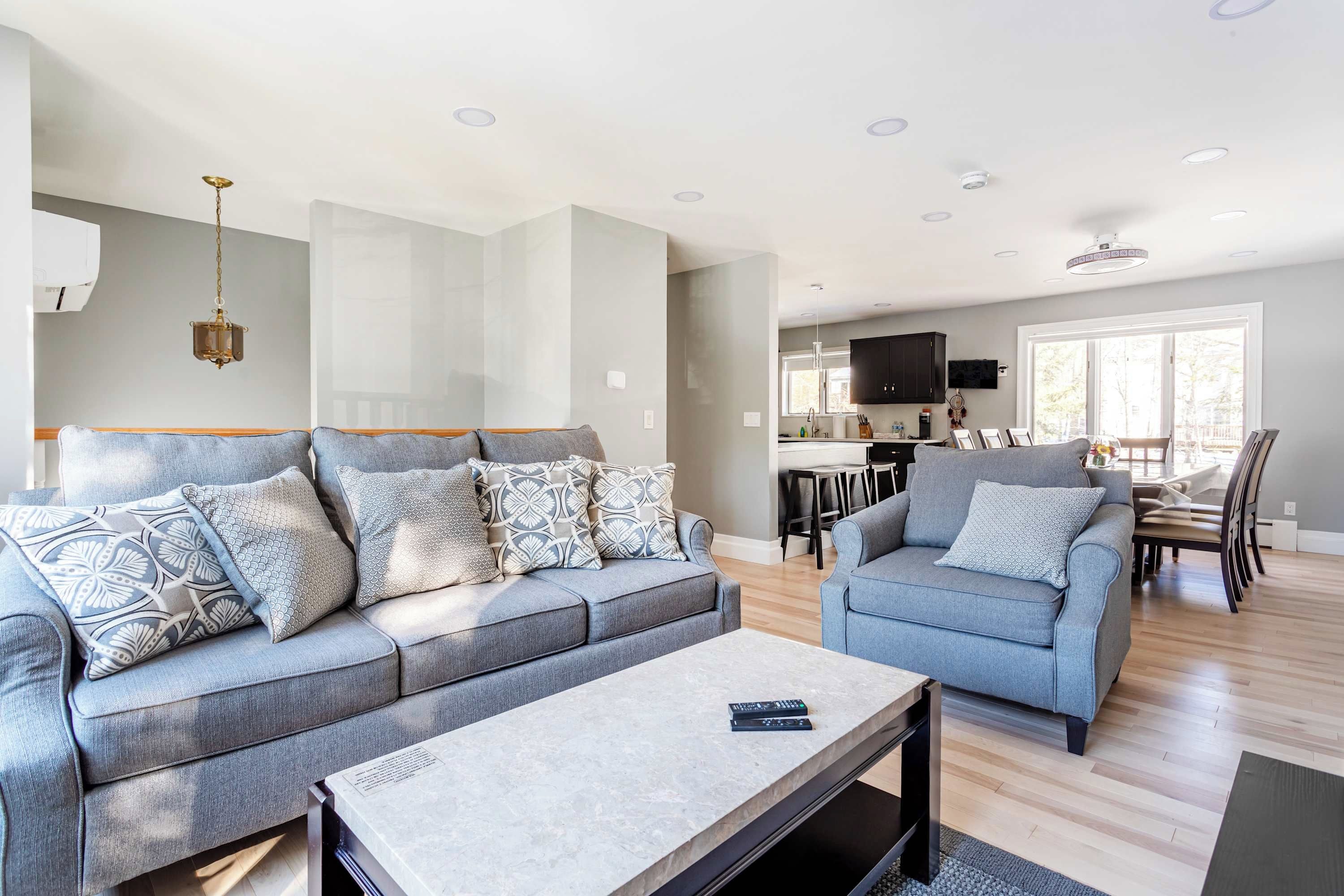 Una sala moderna con un conjunto de sofá gris, una mesa de centro y una zona de comedor, con una televisión y una cocina al fondo.