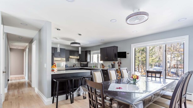 A modern kitchen with dark cabinets, a central island, and a dining area with a glass table and chairs. - The Woodland Escape | Pool Table | Fire Pit | 4 BD (Tobyhanna)