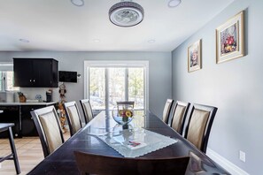 A dining room with a long table, chairs, a vase with flowers, and framed pictures on the wall.