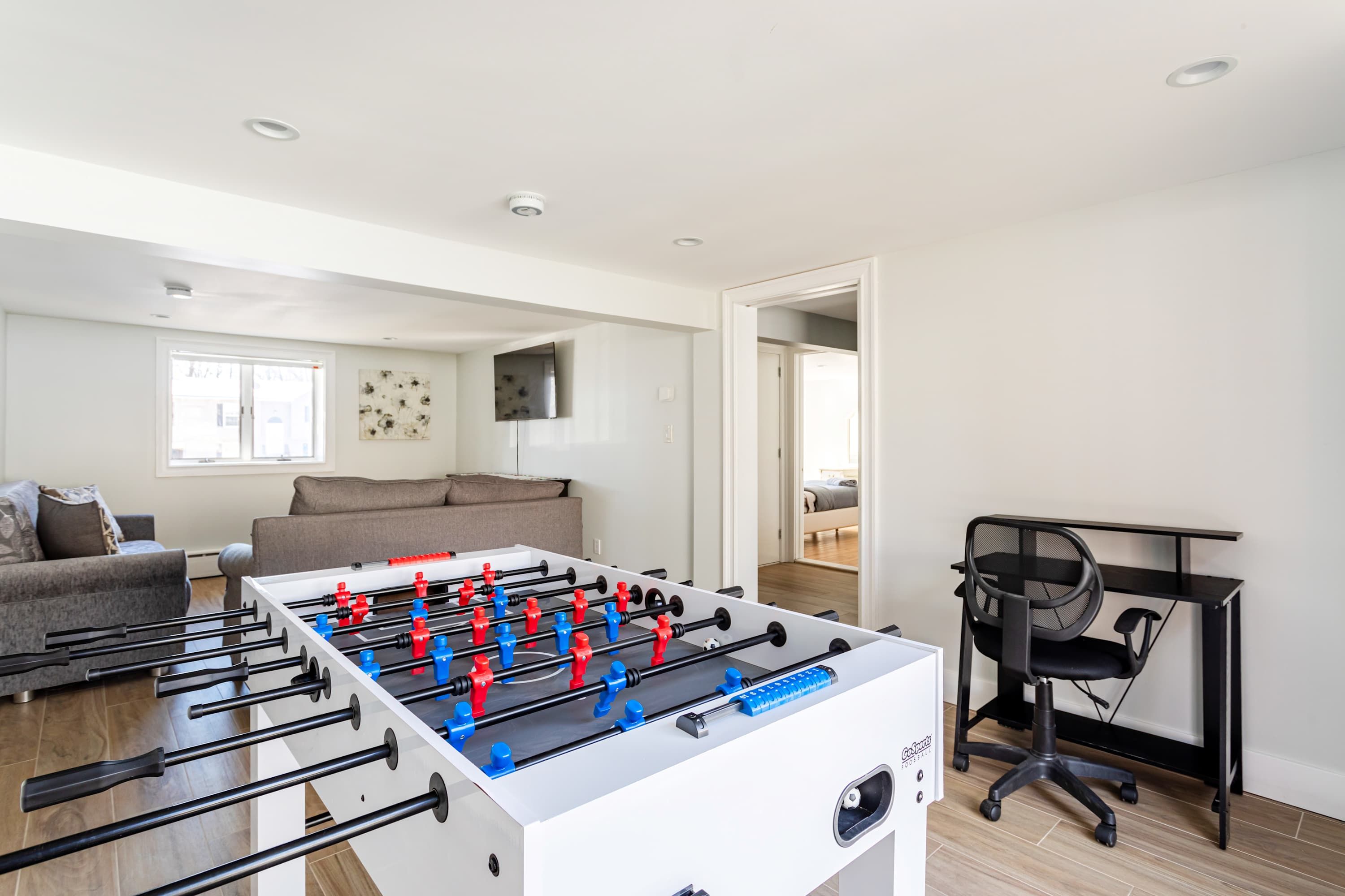 Una sala moderna con una mesa de futbolín, un sofá, un televisor montado en la pared y un escritorio con una silla.