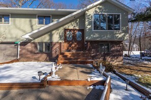 A two-story house with a front porch, a brick foundation, and a snow-covered driveway.