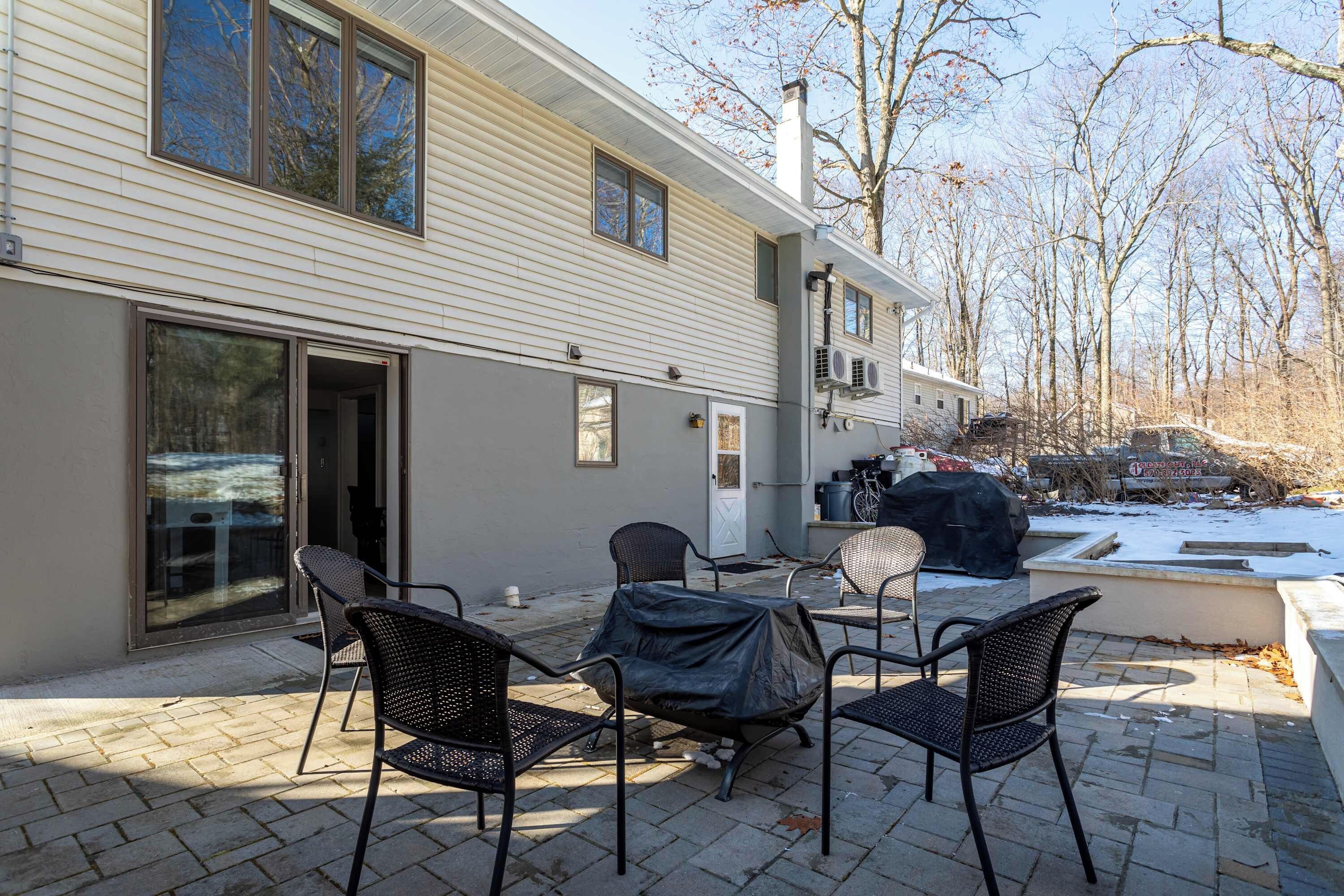 Une terrasse avec des meubles d’extérieur, un barbecue abrité et une cour enneigée.