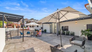 A spacious outdoor patio with stone flooring, outdoor seating, and umbrellas providing shade.