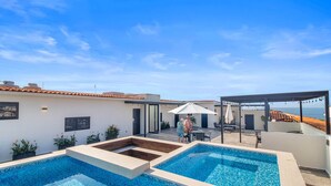 A rooftop pool area with two swimming pools, a covered seating area, and a view of the sea.
