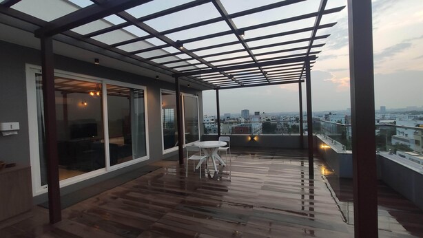 A covered balcony with a wooden floor, glass doors, and a table with chairs. - Trinetra Homes 61 (Bengaluru)