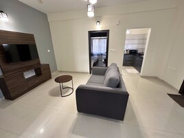 A modern living room with a flat-screen TV, dark wood entertainment unit, grey sofa, and a small round table.