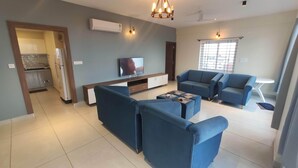 A modern living room with a TV, blue sofas, and a dining area with a table and chairs. - Trinetra Homes 61 (Bengaluru)