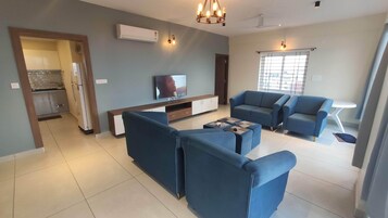 Una sala de estar moderna con televisor, sofás azules y un comedor con mesa y sillas.