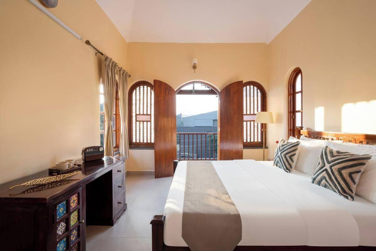 A hotel room with a large bed, a wooden desk, and a view through arched windows.